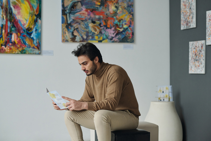 Young man resting on couch and reading brochure at exhibition